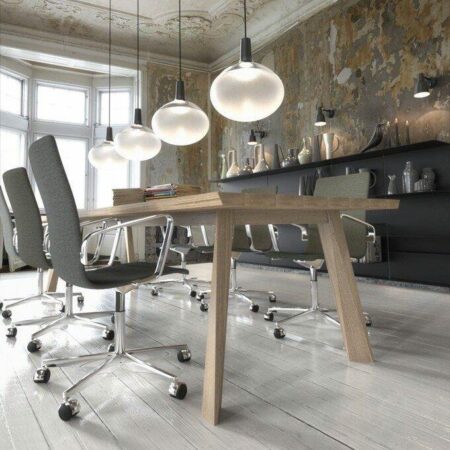 4 Skandinavische Glas-Pendelleuchten über einem Holztisch und 5 Bürostühlen; im Hintergrund ein Sideboard und 3 Wandleuchten an einer Wand im Shabby-Look. Die Decke ist mit Stuck verziert
