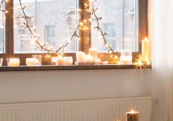 Lichterkette am Fenster, zahlreiche Kerzen auf der Fensterbank und dem Couchtisch