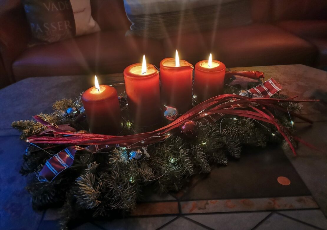 Ein klassischer Adventskranz aus Tannenzweigen, geschmückt mit roten Ornamenten, 4 brennende rote Kerzen